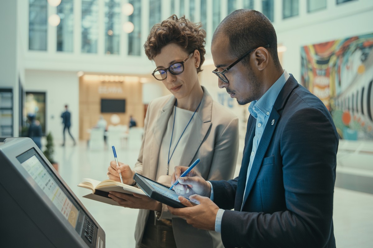 Deux salariés vérifient leurs cotisations URSSAF sur un kiosque interactif public lumineux
